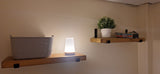 Wooden shelves with a basket, lamp, and plant against a beige wall.