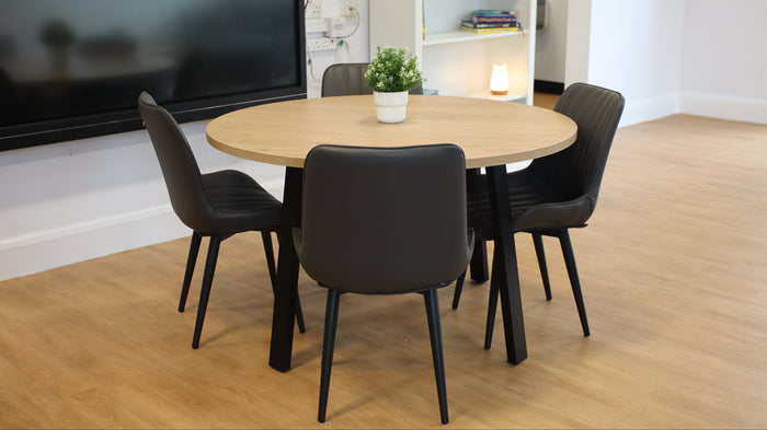 Round wooden table with four black chairs in a room with a TV and shelves.