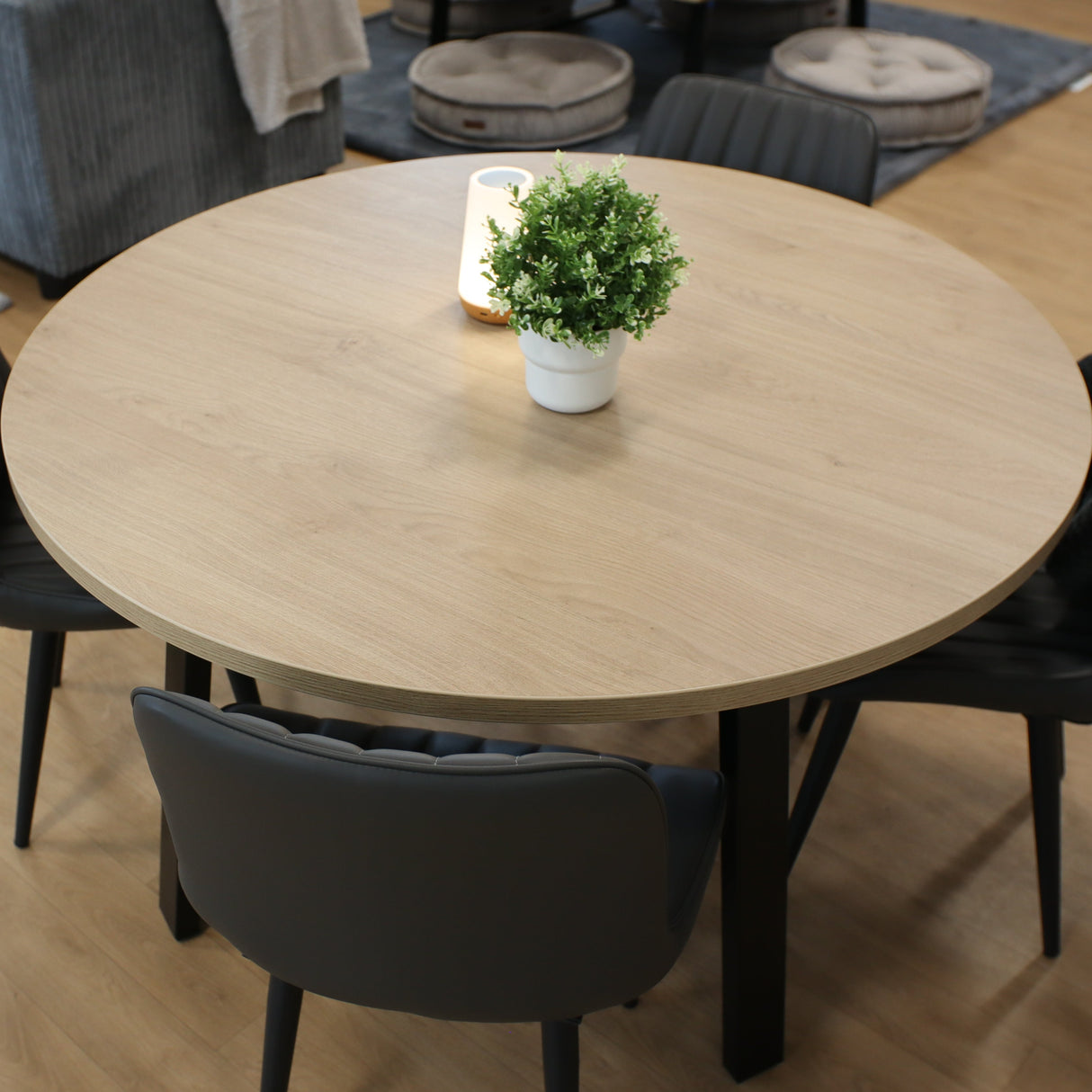 Round wooden table with four black chairs in a classroom with gray sofa and poufs.