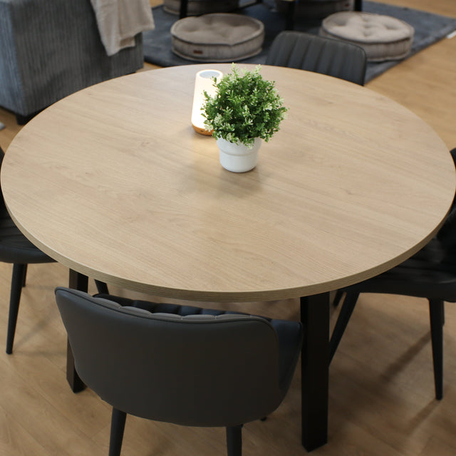 Round wooden table with four black chairs in a classroom with gray sofa and poufs.